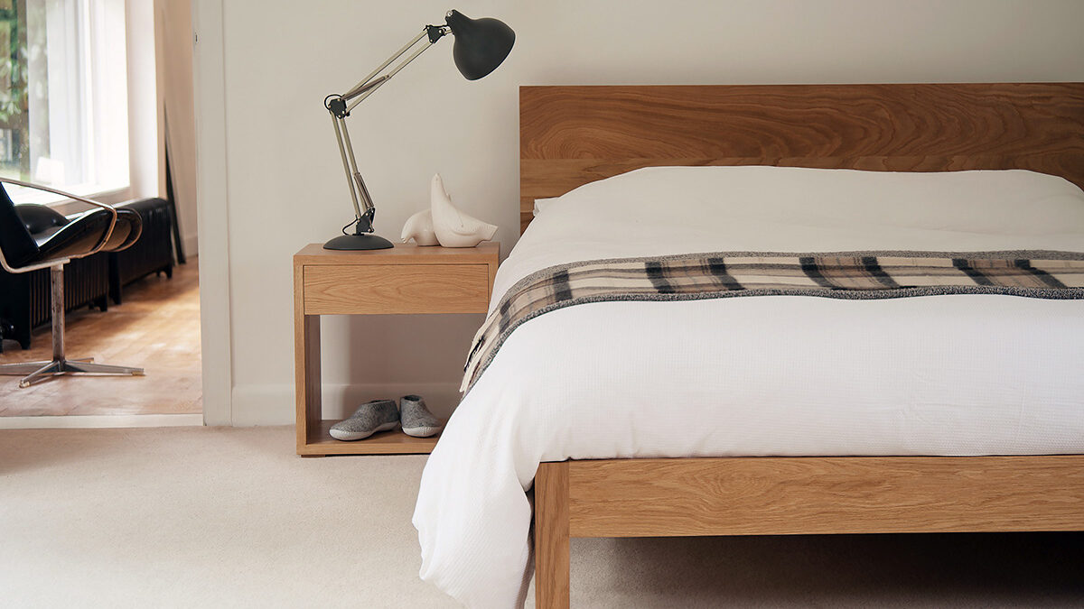 A modern solid wooden bed - the Malabar in Oak and shown with Oak Bedside Cube table