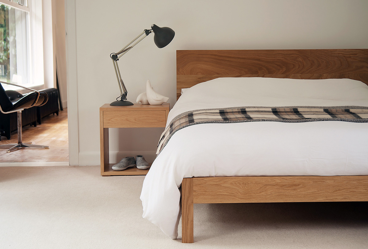 A modern solid wooden bed - the Malabar in Oak and shown with Oak Bedside Cube table