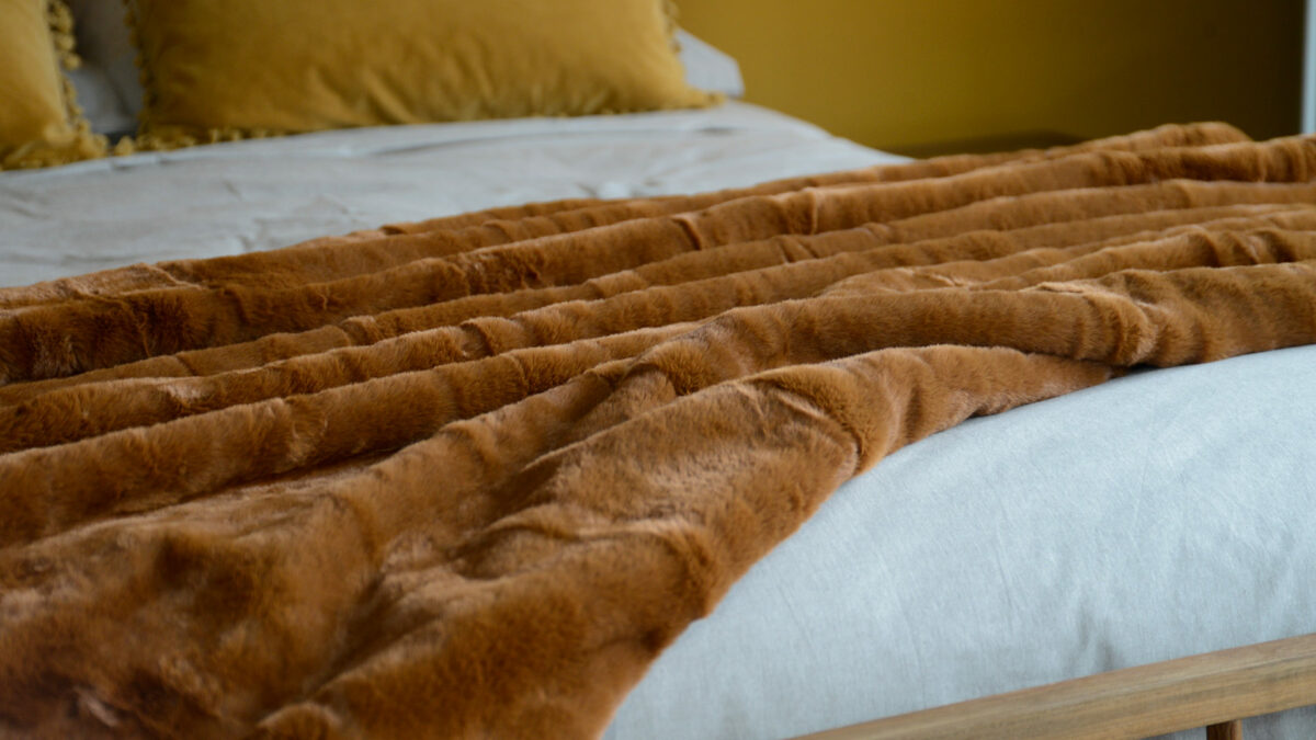 soft and luxurious faux fur throw in a warm tan colour shown draped on a kingsize bed