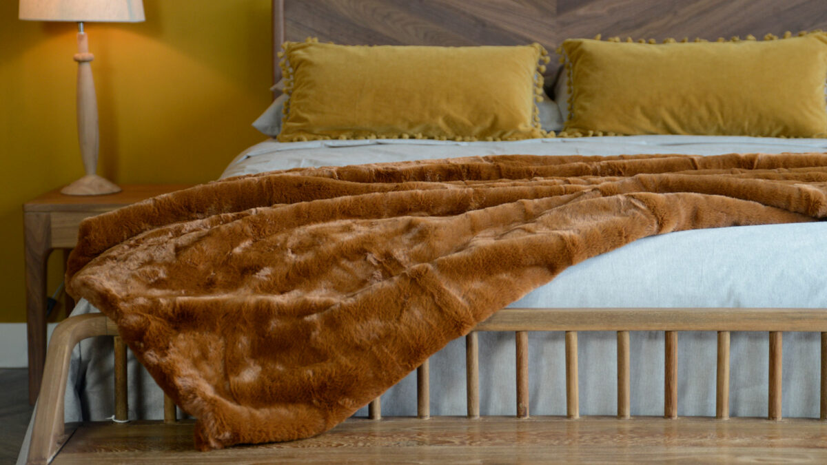 soft and luxurious faux fur throw in a tan colour shown draped on a bed