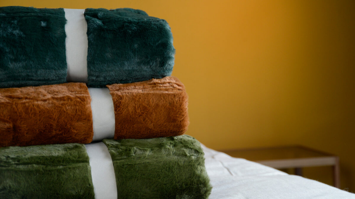 a stack of soft and luxurious faux fur throws in a choice of 3 colours teal, green and tan