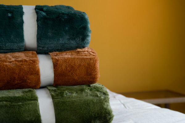 a stack of soft and luxurious faux fur throws in a choice of 3 colours teal, green and tan