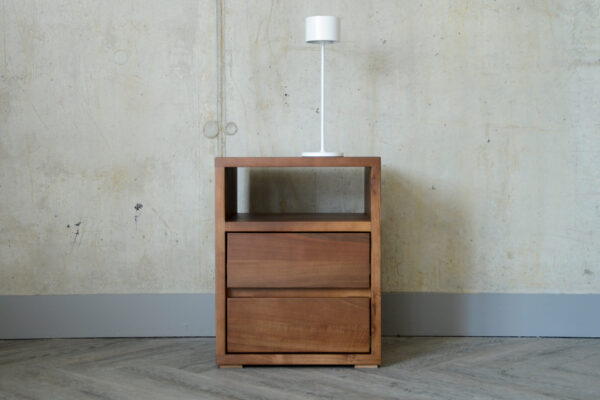 A Black Lotus 2 Drawer Shelf Bedside Table in solid walnut, with its shelf located above the drawers and a white mobile LED lamp sat on top of the table.