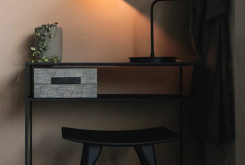 Black metal console table with black stool. Large black desk lamp and small house plant on top.