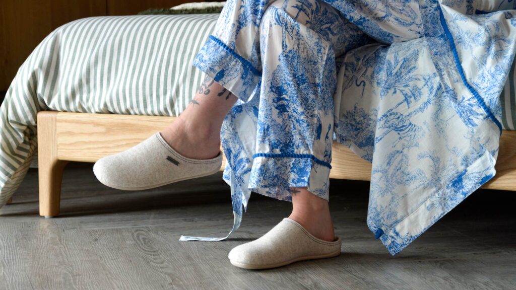 model wearing blue and white jungle print PJs and robe with clay coloured felt slippers.