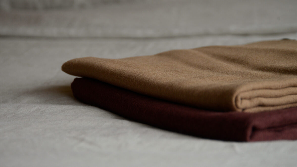 caramel and wine coloured woollen large throws shown folded in a stack