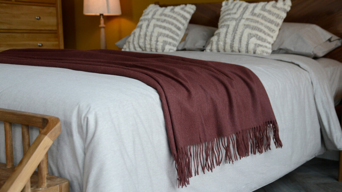 90% recycled Alpaca/wool mix throw in plum shown on a kingsize bed