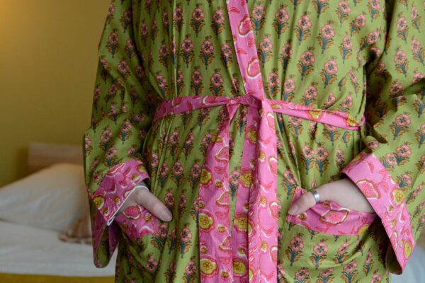 Image showing cropped view of green and pink floral robe on model. Image shows model with hands in pockets of robe, and pink trim found on the edges of the robe, sleeve cuffs and pockets.