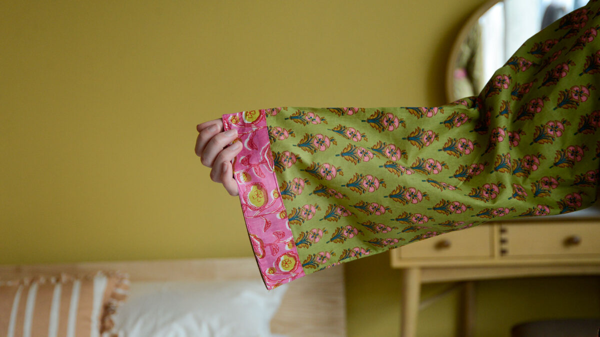 Image showing sleeve detail on green and pink floral robe. Model is holding one arm out to show the pink trim detail on the end of the robe's sleeve.