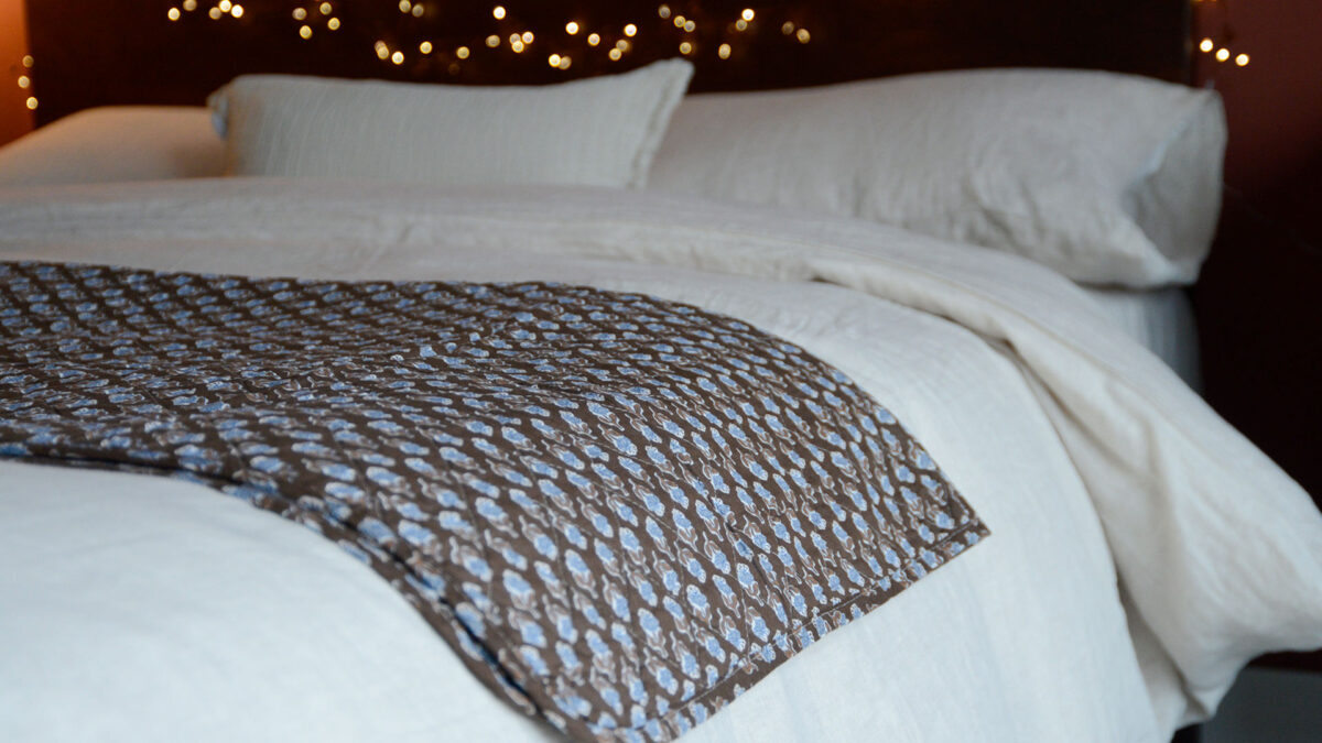 Brown Quilted Throw with Blue Flowers over Linen Bedding