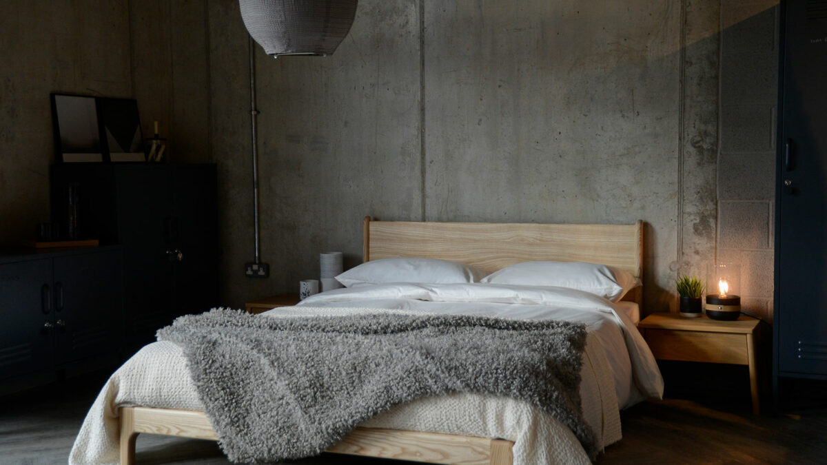 A low hand made Arts and Crafts style wooden bed, in an industrial bedroom setting, the Carnaby in solid ash