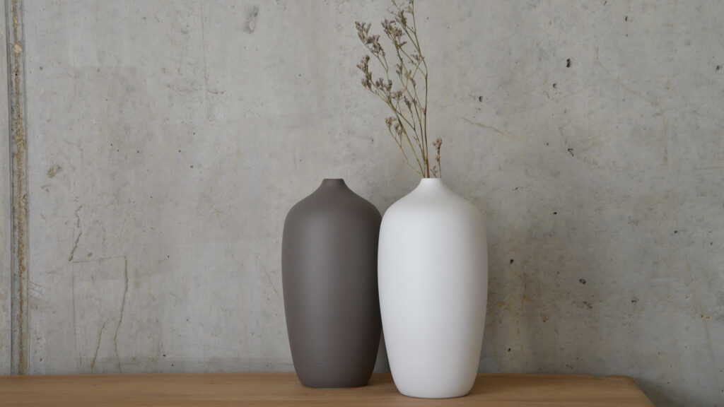Large grey and white vases with small openings stood together against concrete wall.