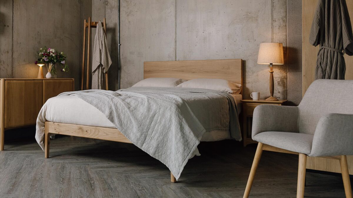 A low angled shot of the English oak Chiswick, dressed in the organic linen bedding in ecru. The bedding is mostly covered up by a embroidered striped bedspread in the colour silver-grey, which also overhangs the bottom right-hand corner of the bed base.