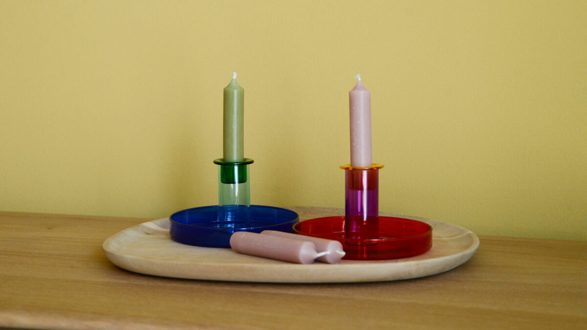 Colourful glass candleholders. To the left, a glass candleholder is shown in dark, rich blue with a blue candle. To the right, another candleholder sits in a bright crimson red colour with a pink candle.