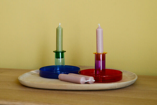 Colourful glass candleholders. To the left, a glass candleholder is shown in dark, rich blue with a blue candle. To the right, another candleholder sits in a bright crimson red colour with a pink candle.