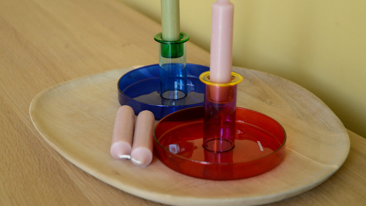 Colourful glass candleholders with pink candles to the left hand side. All arranged on a wooden oak tray.