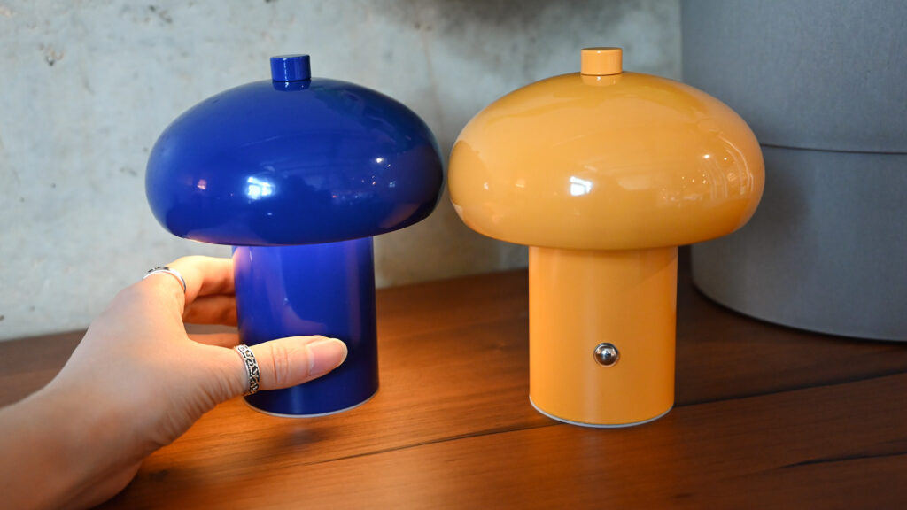 Colourful retro style rechargeable lamps in blue and yellow with a hand holding the blue lamp on the left, to demonstrate the scale.