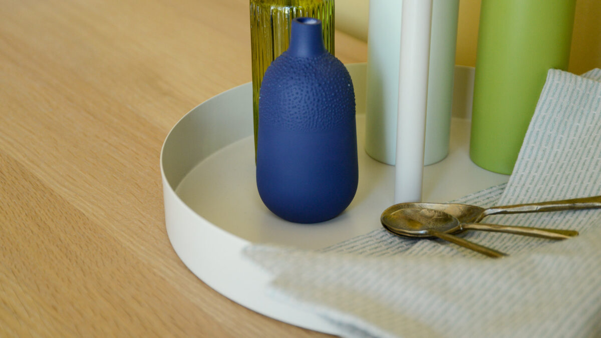 Close up of round metal green tray carrying a blue vase, iron spoons and green salt and pepper grinders.