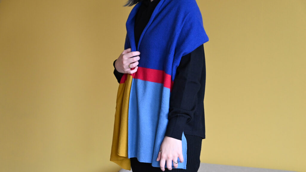 Model wearing striped colour block scarf in blue, mustard, and red.