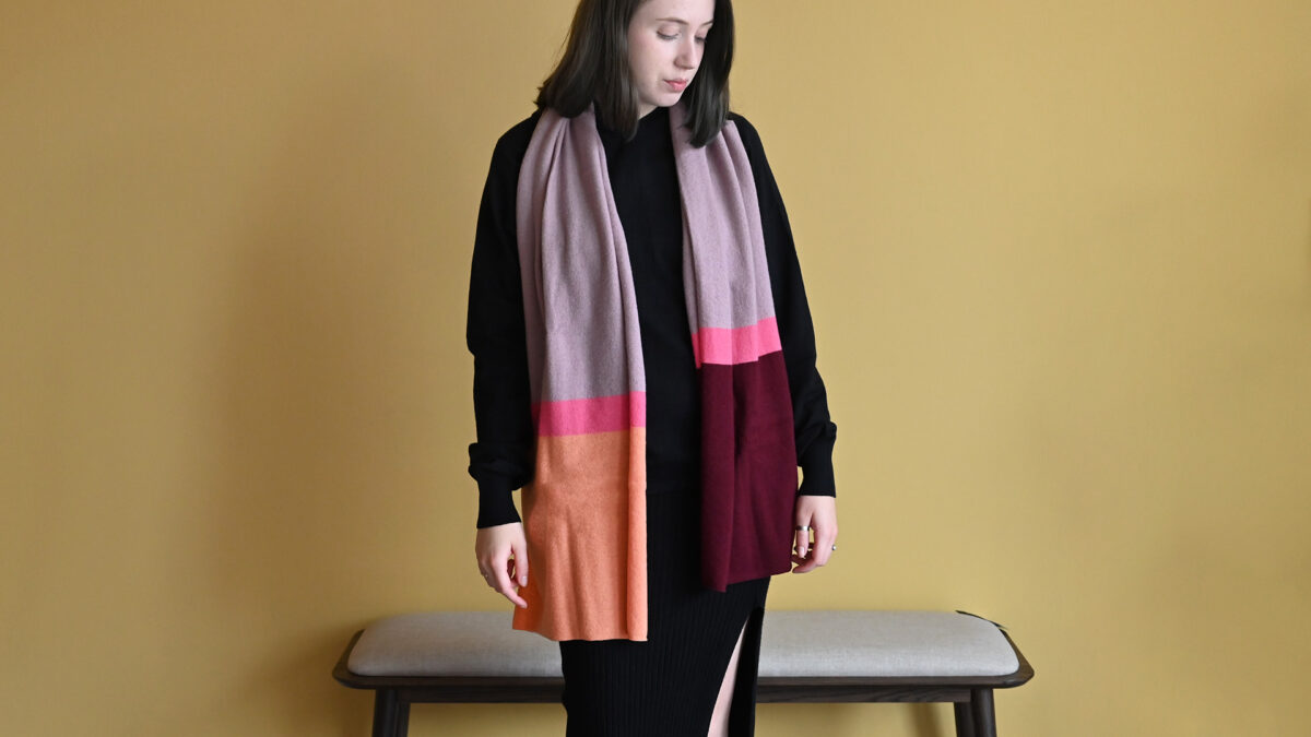 Model wearing Colourful scarf in orange, pink, purple and maroon stripes.