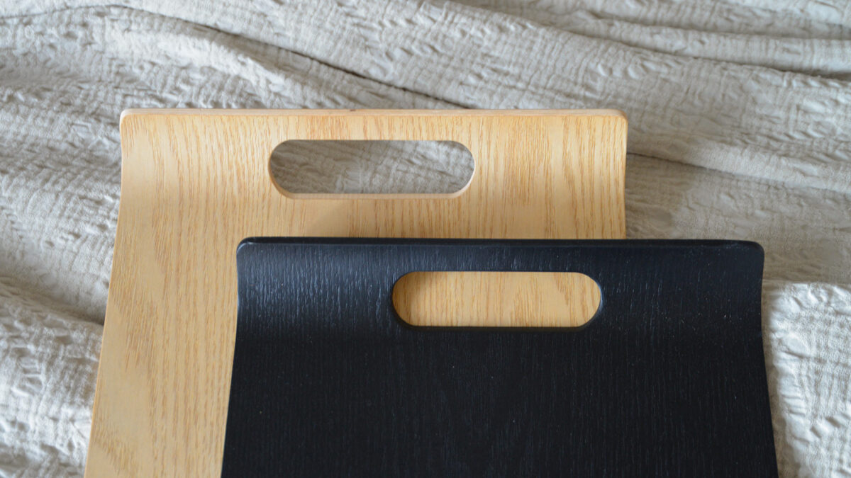 close up of a black curved tray, on top of an oak curved tray.
