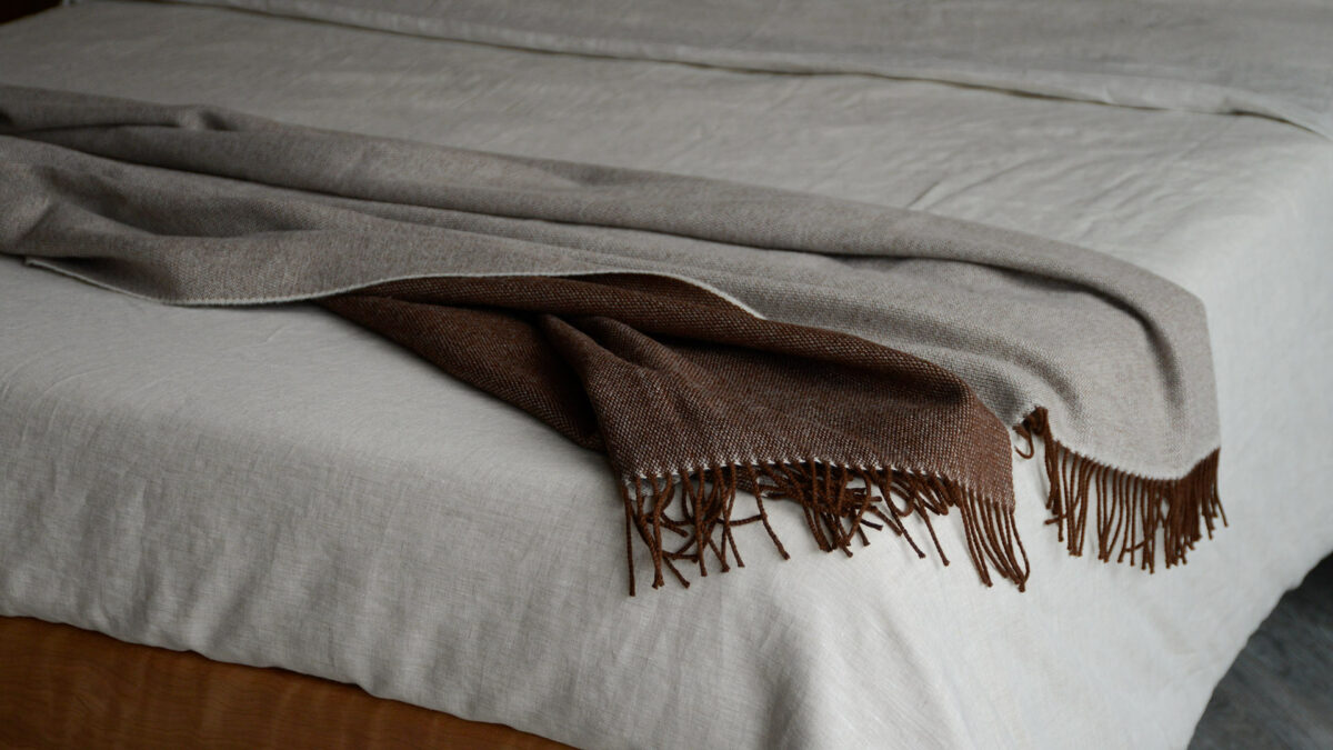 large brown and beige reversible lambswool throw shown draped on a bed