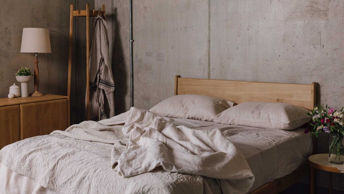 Bedroom scene with oak side board and coat stand. English oak bed centre of shot, with rumpled ecru bedding and throw.