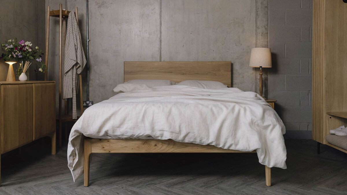modern oak bed with neutral bed linen. Oak sideboard, bedside table, clothes rail and coat stand surrounding.
