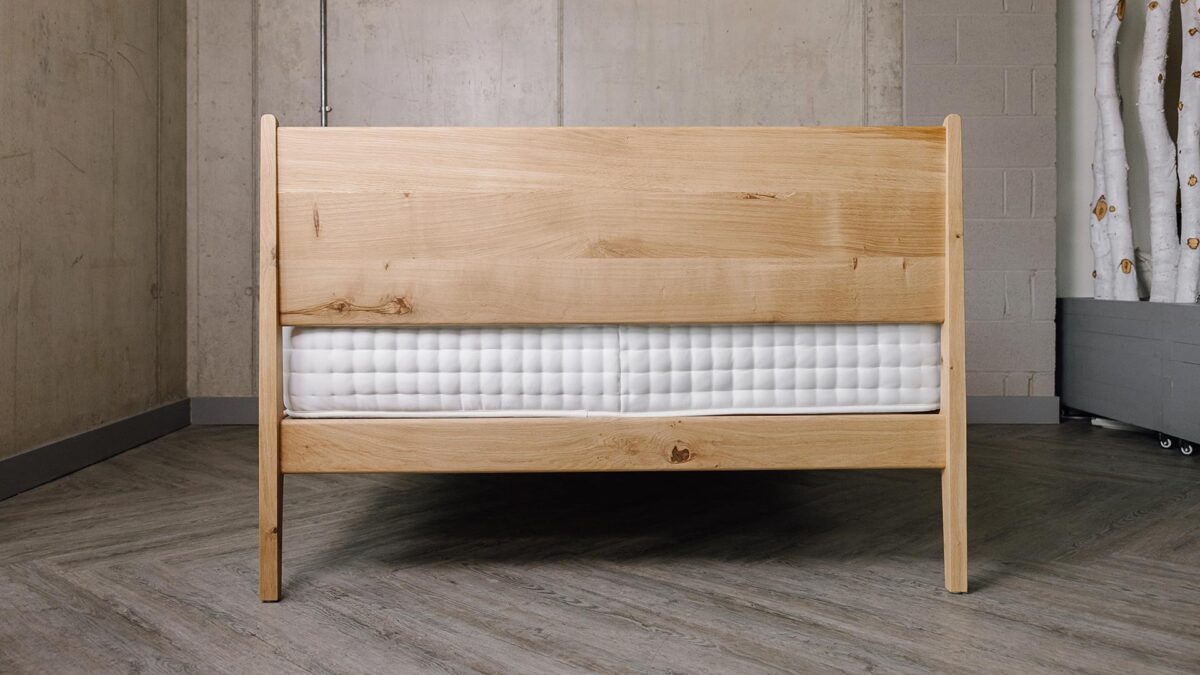 Back of English Oak Camden Bed. Legs, mattress gap, mattress and back of headboard in shot. Knots visible in headboard and headboard rail.