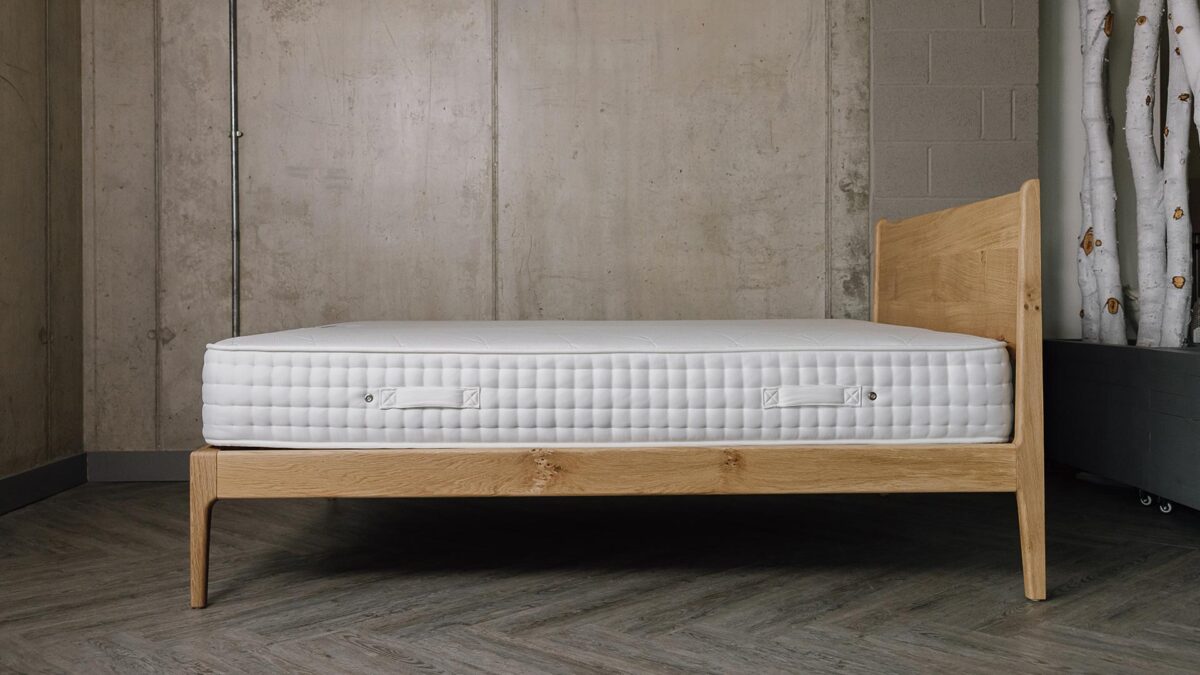 Side view of an English oak bed frame with a mattress.