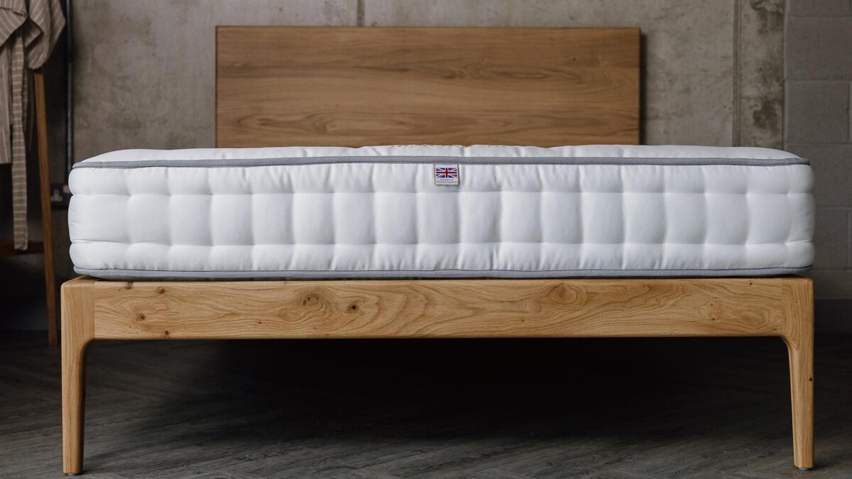 A low forward facing shot of the English oak Chiswick bed base, focusing on the foot-rail/leg section of the bed. The bed has a bare mattress on top of it.