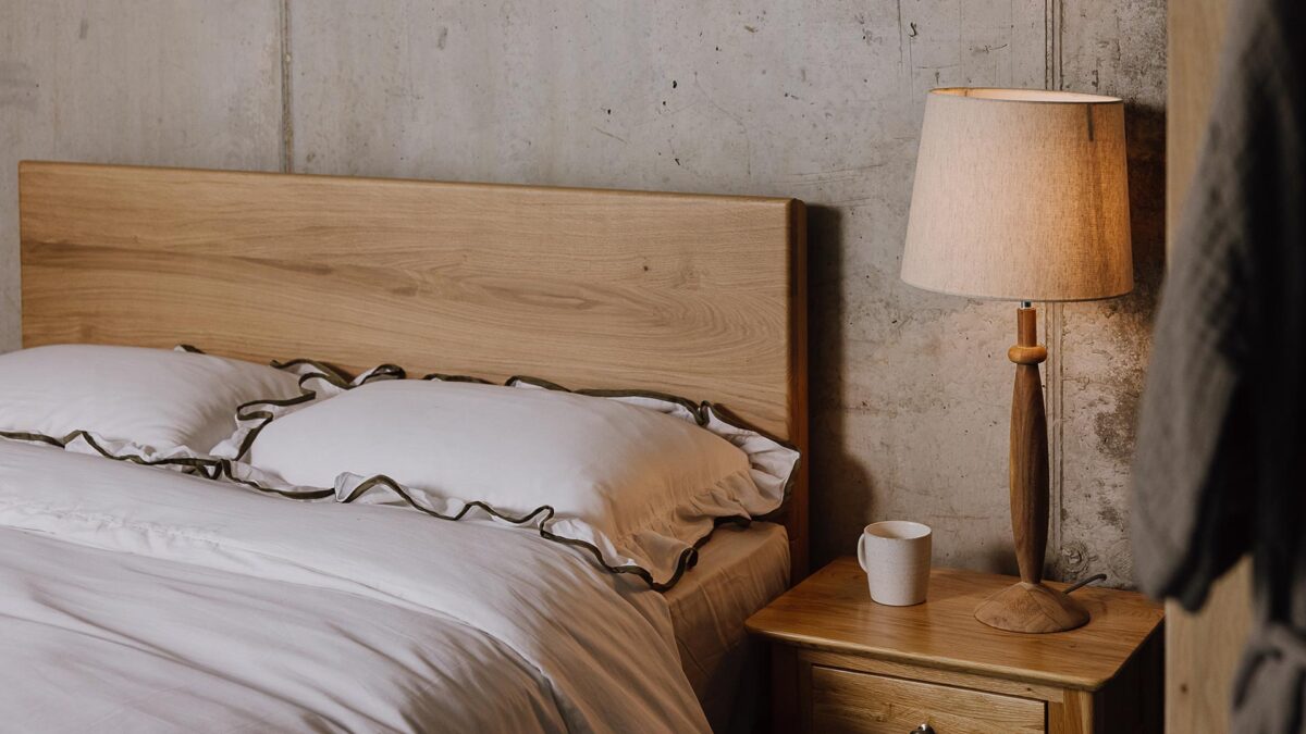 A close up angled image of the English oak Chiswick. The image focuses on the headboard panel. The bed is dressed in the white bedding with green ruffled border.
