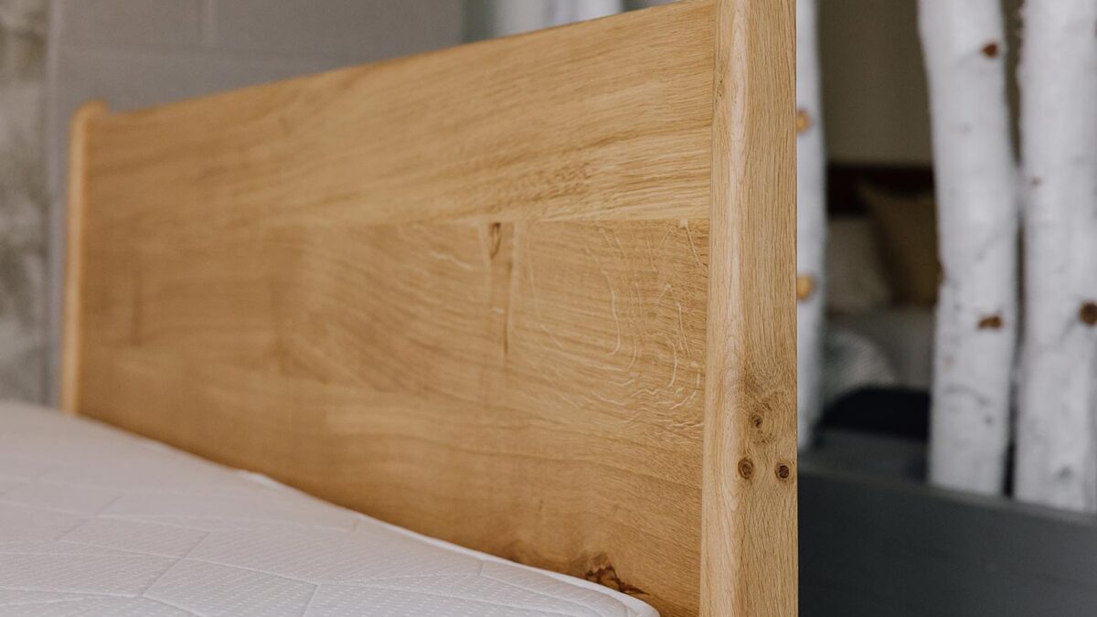 side view of Camden headboard, focus on headboard legs. Knots and cats paws visible in the English oak.