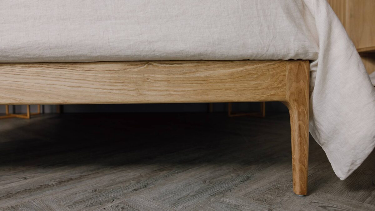Close up of the English oak Camden's foot-rail. The bed is dressed in the organic linen bedding in ecru.