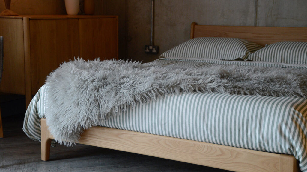 Image showing the faux afghan throw spread over the Pimlico bed, which is also dressed in green and white striped bed linen.