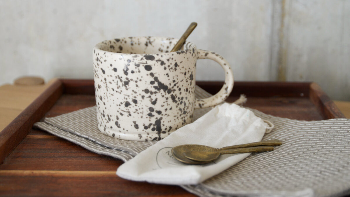 Forged iron spoons pictured with a grey and white mug and a dark wood tray.