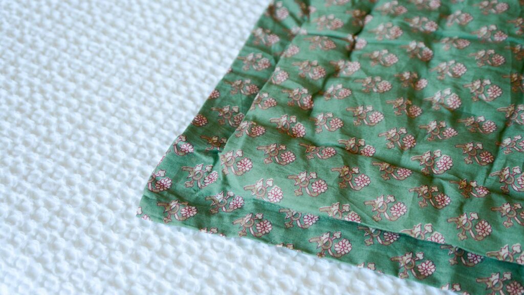 Image shows the corner of a green quilted throw with a padded inner and thin border.