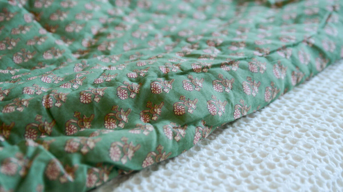 Closeup image of green floral quilted throw, folded over on top of a white bedspread.