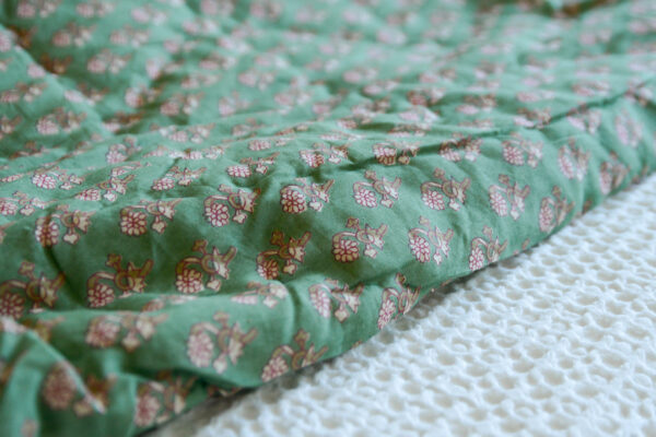 Closeup image of green floral quilted throw, folded over on top of a white bedspread.