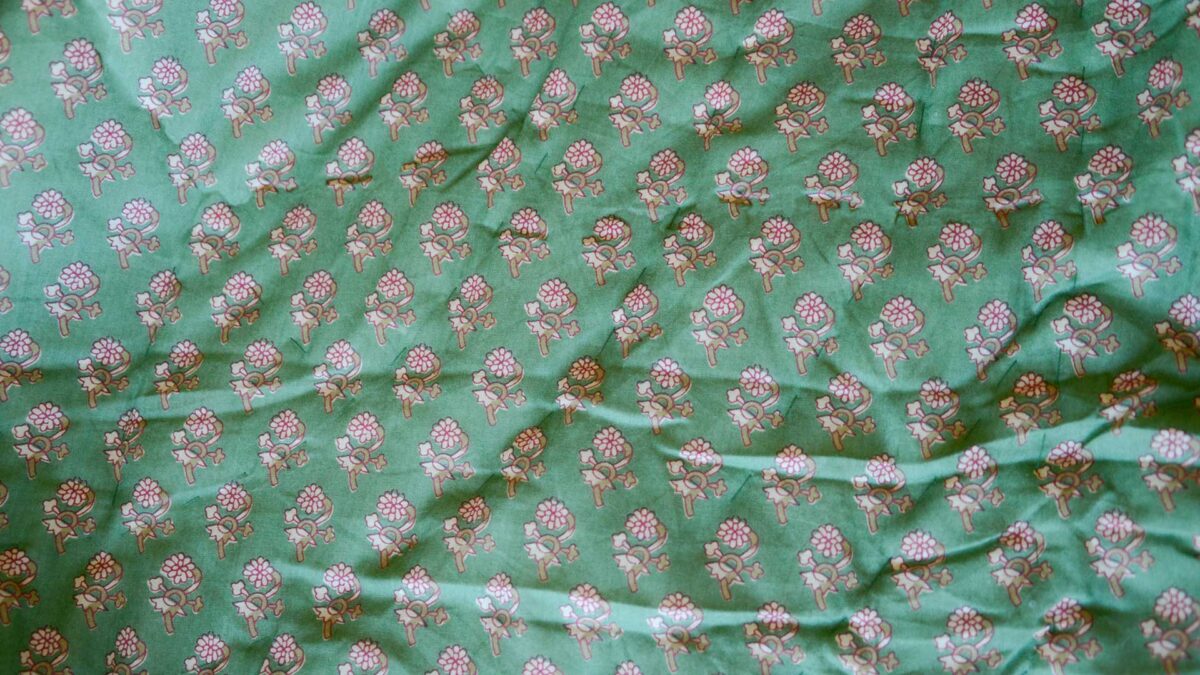 Closeup of green floral quilted throw. Image shows detail of the pattern on the throw, which includes fine line drawings of modern flowers in a dark red and shades of pale beige.