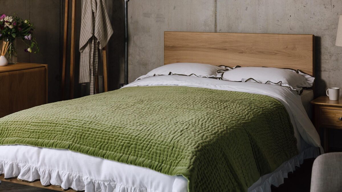 An angled shot of the English oak Chiswick, dressed in white bedding with a ruffled border with green detailing. Over top of the bedding is a green stitched velvet throw.