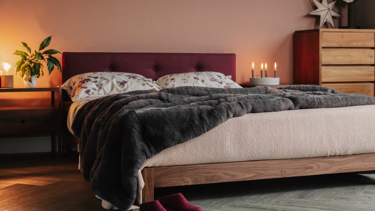 Iona low wooden bed in walnut with upholstered headboard in berry coloured wool fabric