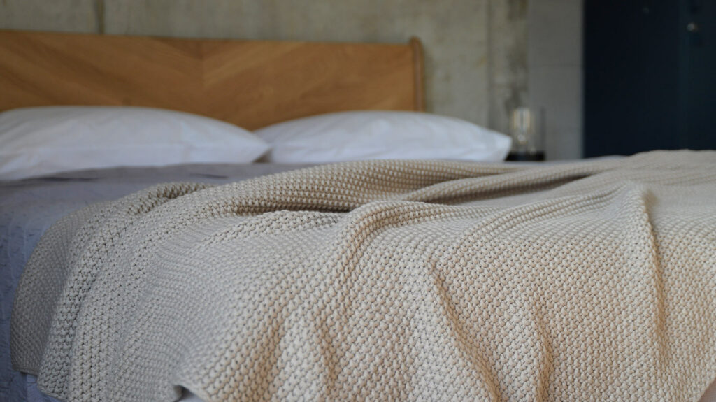 moss stitch knitted cotton throw in taupe shown on a bed