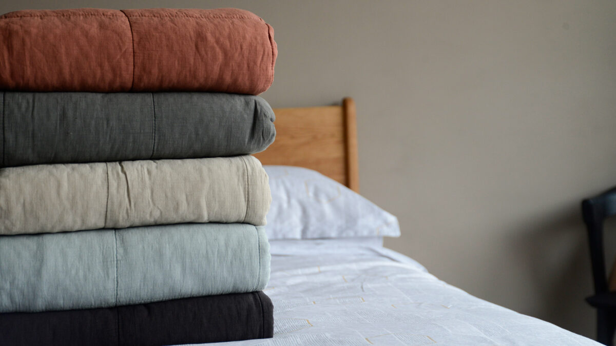 a stack of large soft quilted bedspreads in a choice of colours