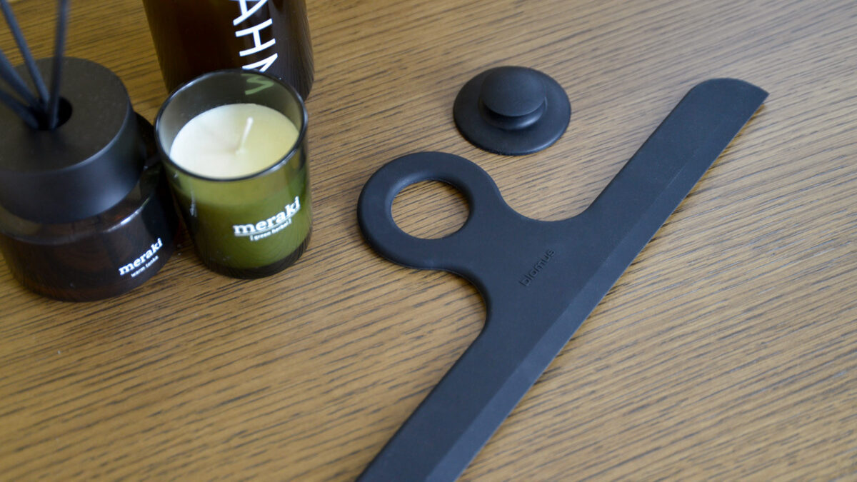 black shower wiper with hanger next to a candle and diffuser.