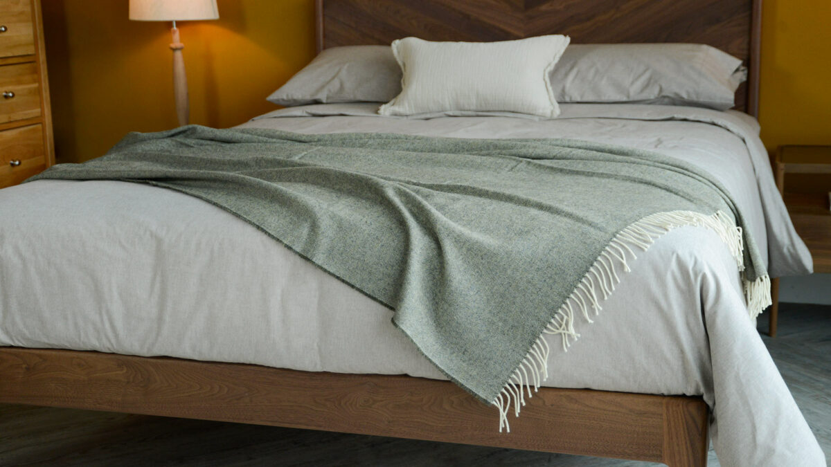 Moss green Herringbone weave lambswool throw shown draped on a bed