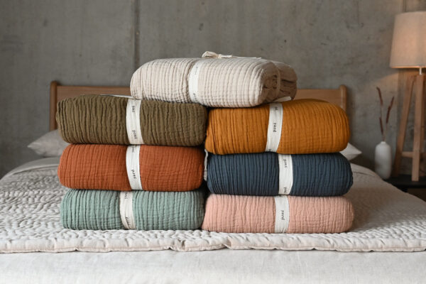 Muslin bedspreads in various colours, neatly folded and stacked.