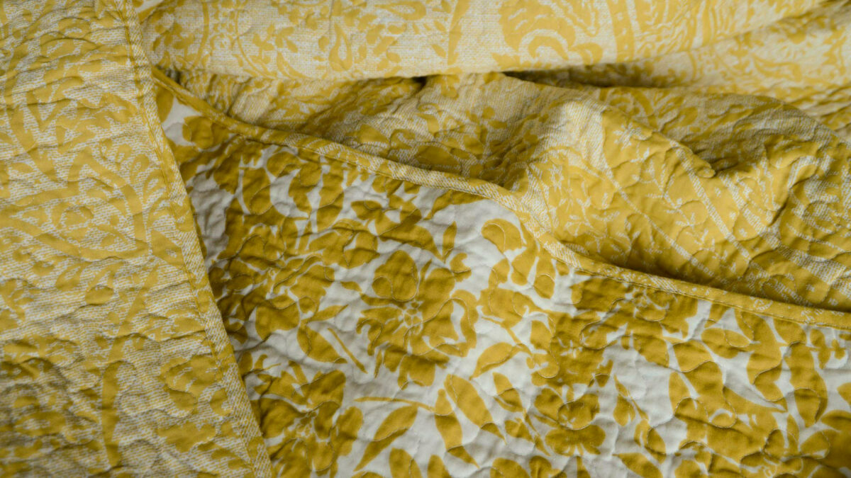 reversible printed floral pattern quilted bedspread in ivory and yellow ochre a close up view showing both sides