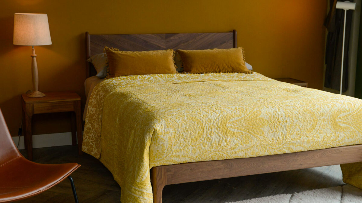 reversible printed floral pattern quilted bedspread in ivory and yellow ochre shown on a Kingsize wooden bed