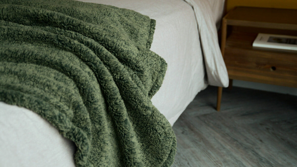 Olive green marl soft and cozy fleecey throw shown draped on a bed